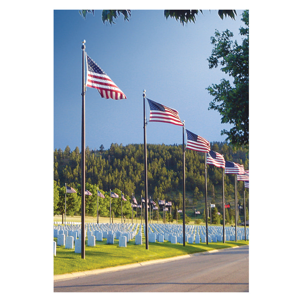 A row of American flags waving over a cemetery with white gravestones and green hills in the background