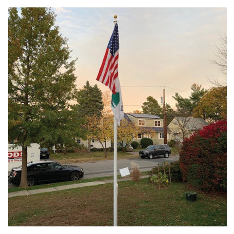 America flag above an unknown white flag on a flagpole in the sky in front of a neighborhood