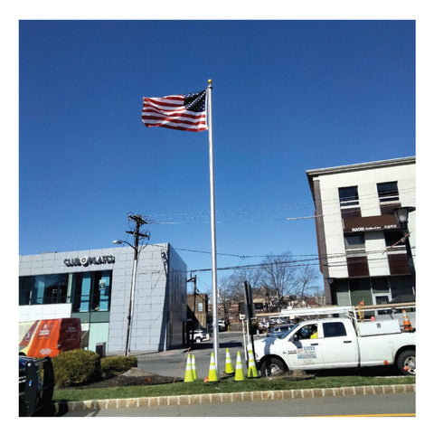 American flag on a pole waving in the sky in front of two buildings