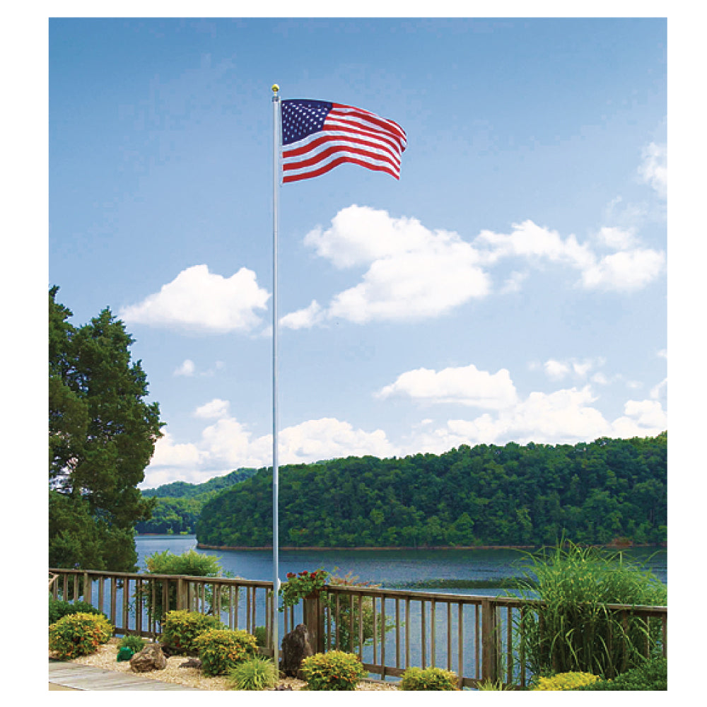 America flag waving on a flagpole in the sky in front of a lakefront and trees